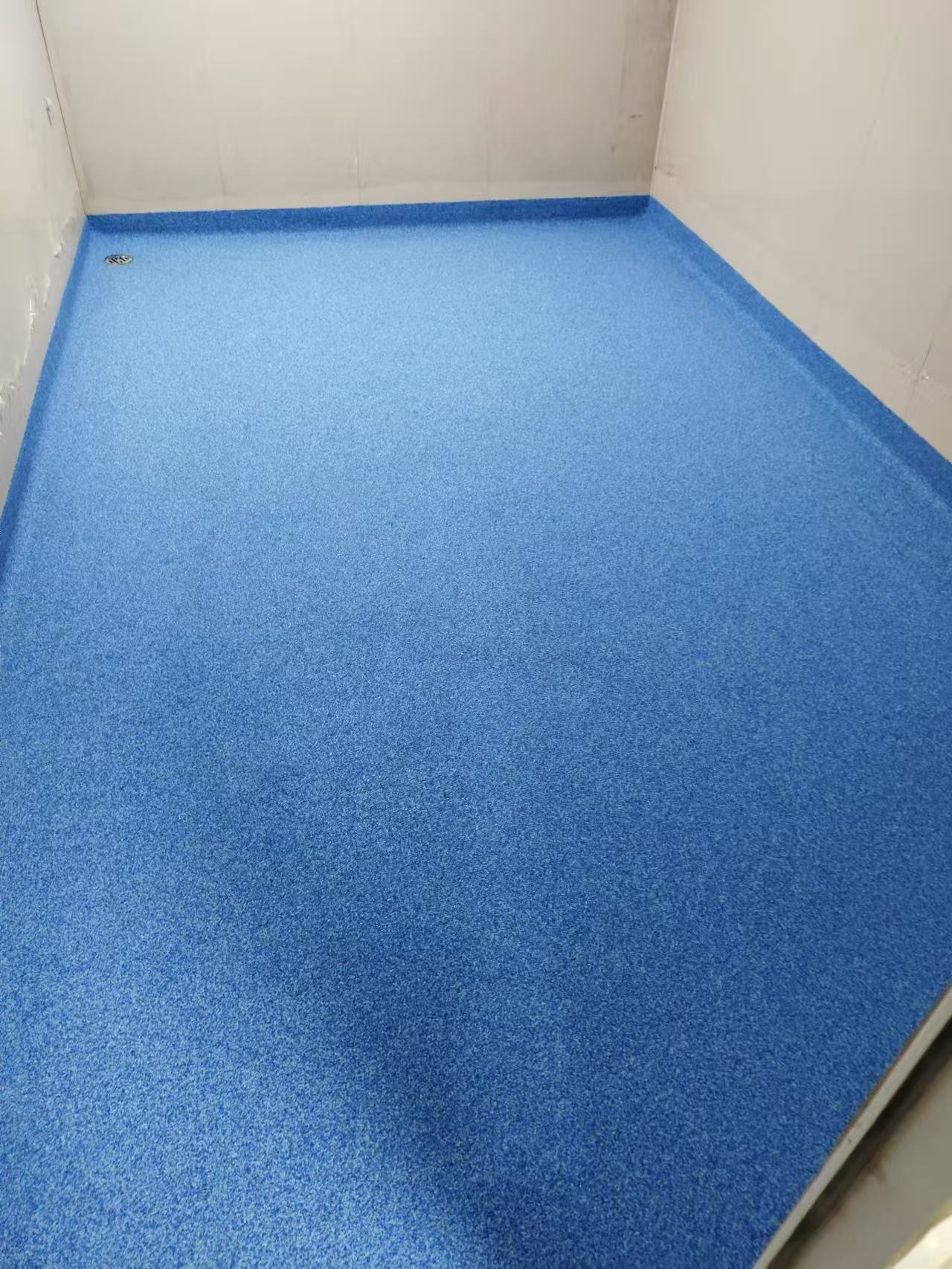 Blue speckled resin floor with perimeter coves and a drain